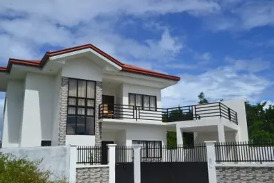 White two storey house with a red roof edge, stone accent wall, terrace railing and metal gate