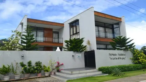 White two storey house with wood accent panels and balconies, perimeter wall carrying painted lettering
