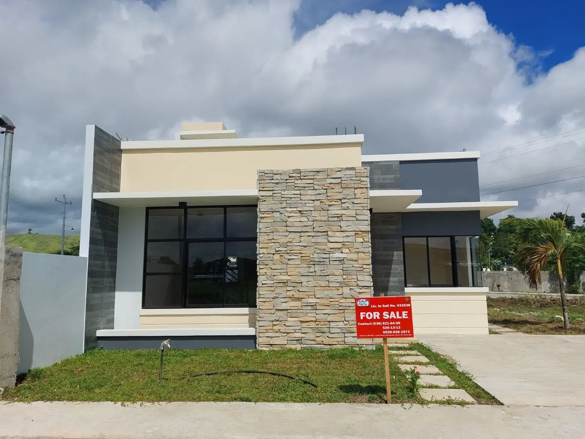 Single storey house with stone veneer column and dark windows, red For Sale sign on the front lawn