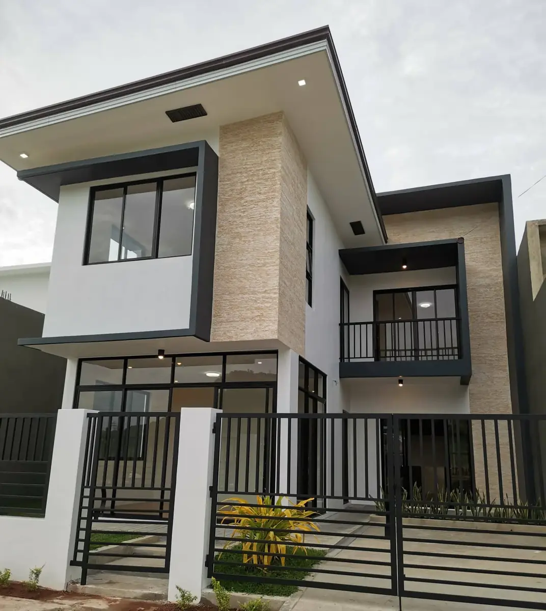 Two storey house with stone clad wall, dark framed windows, balcony and a black fence