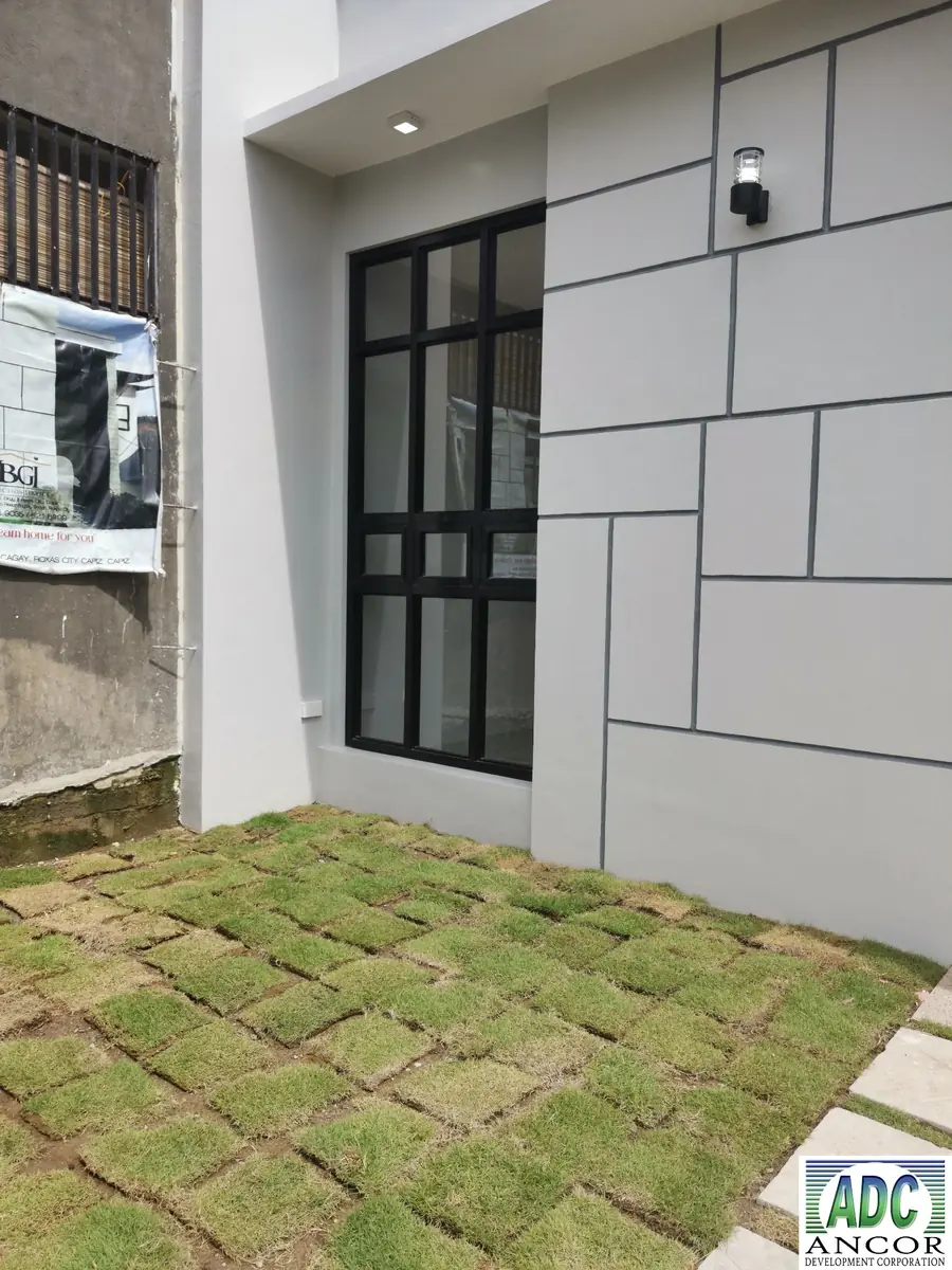 Side yard with grass block paving, black grid window, and wall lamp on panelled grey wall