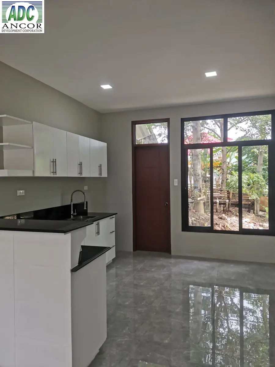 Kitchen with white upper cabinets, black counter, sink, wooden back door, and glossy grey tile floor