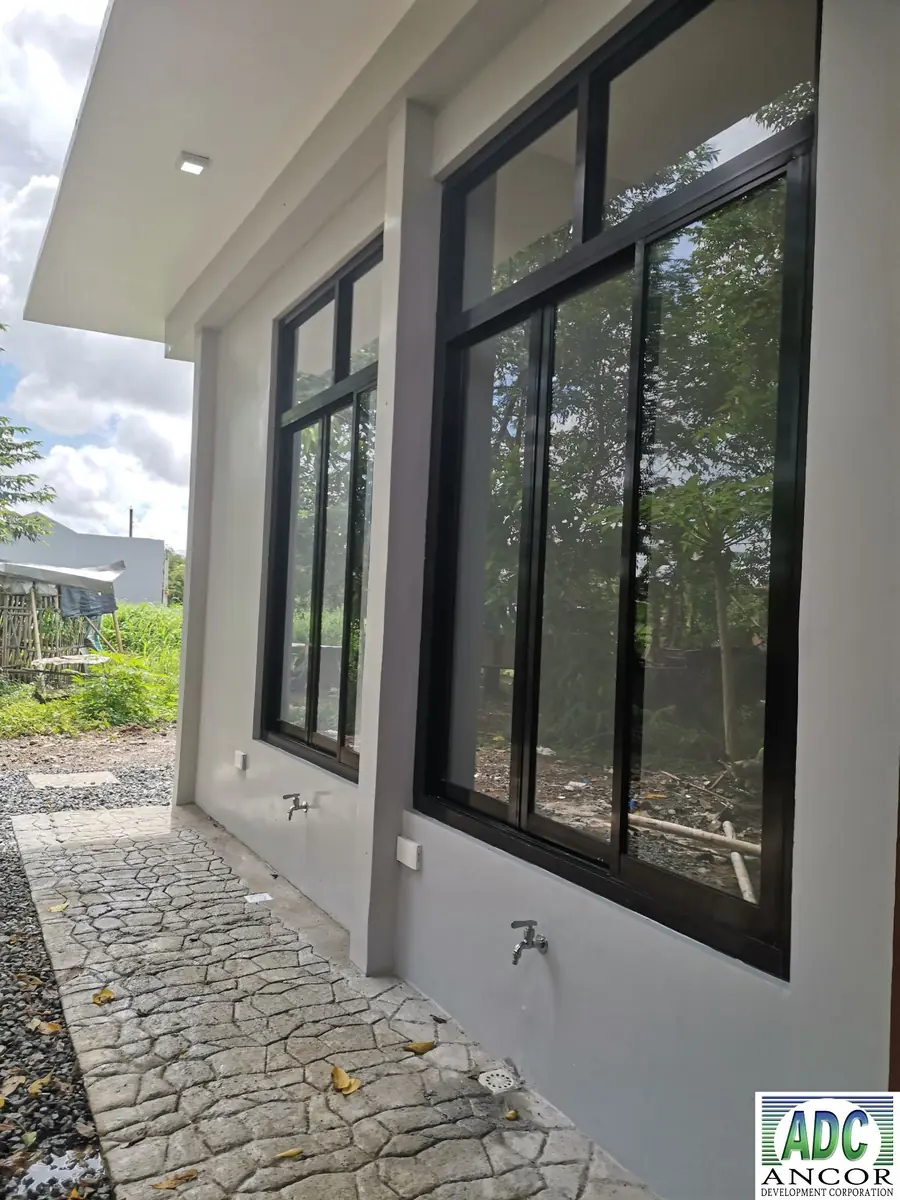 Covered side walkway with stone pattern paving, black framed windows, and outdoor faucets