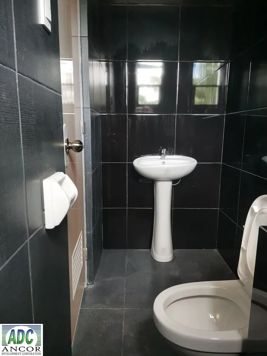 Toilet and bath with black gloss wall tiles, white pedestal sink, toilet, and wall bidet spray