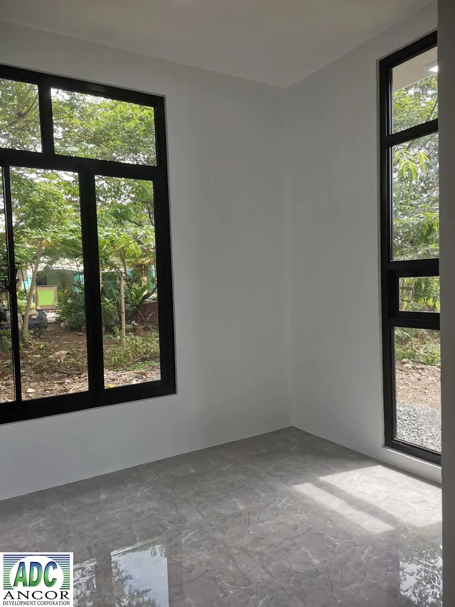 Empty corner room with two black framed windows looking onto trees and glossy grey marble look tile