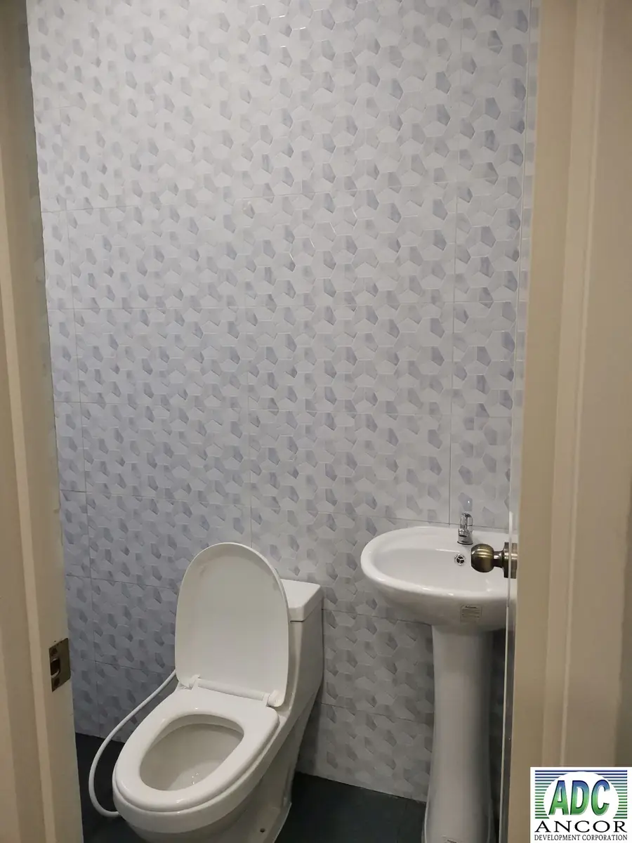 Toilet and bath with white and grey patterned wall tiles, toilet, and white pedestal sink