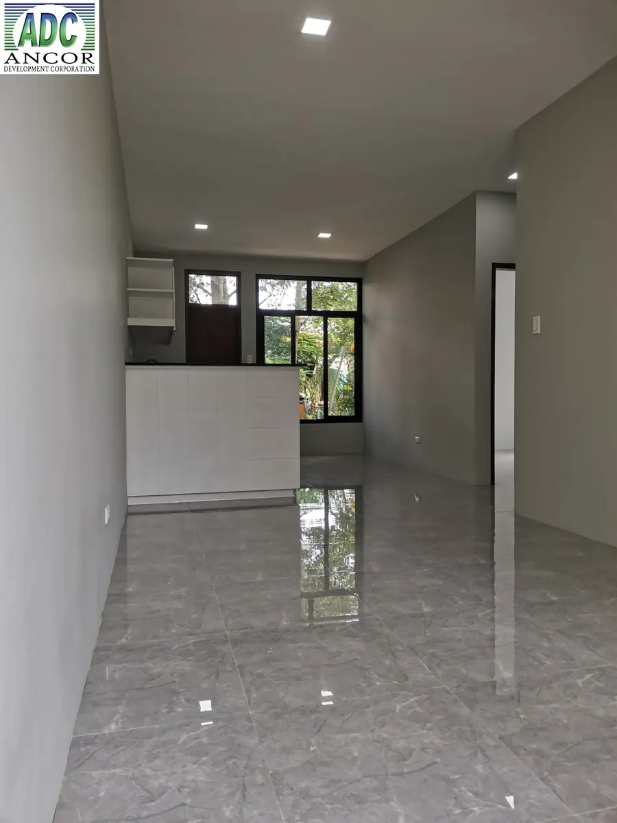 Open living and dining area with white kitchen counter, black framed windows, and glossy grey tile floor