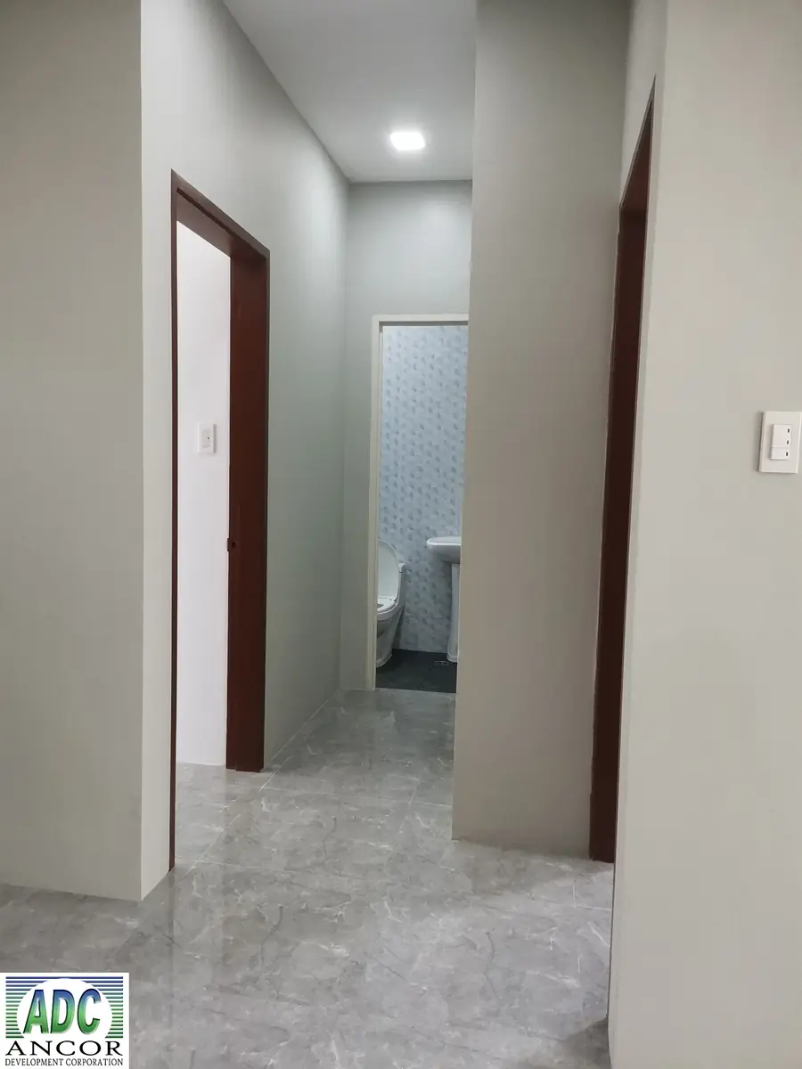 Hallway with wood trimmed doorways leading to a tiled toilet and bath, glossy grey tile floor
