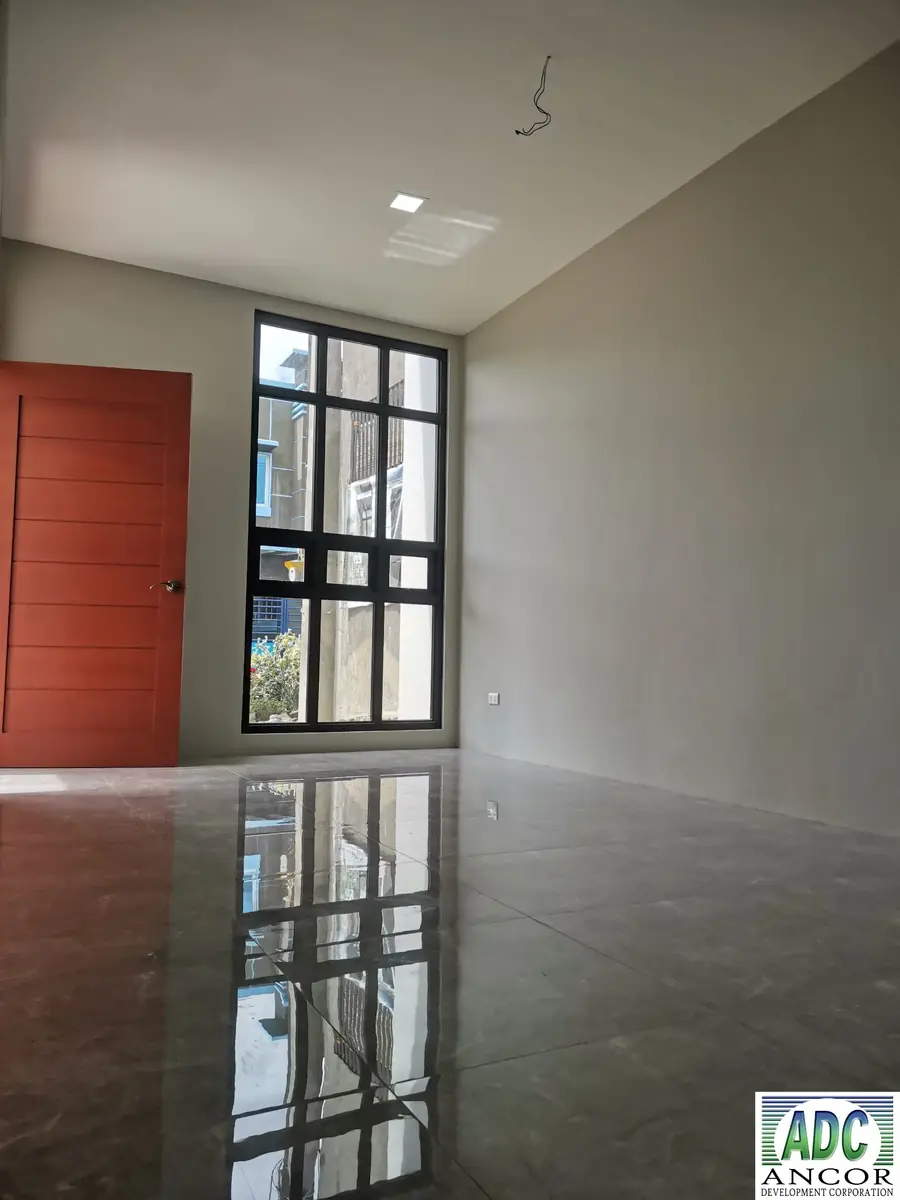 Empty room with red door, tall black grid window, high ceiling, and polished grey tile floor