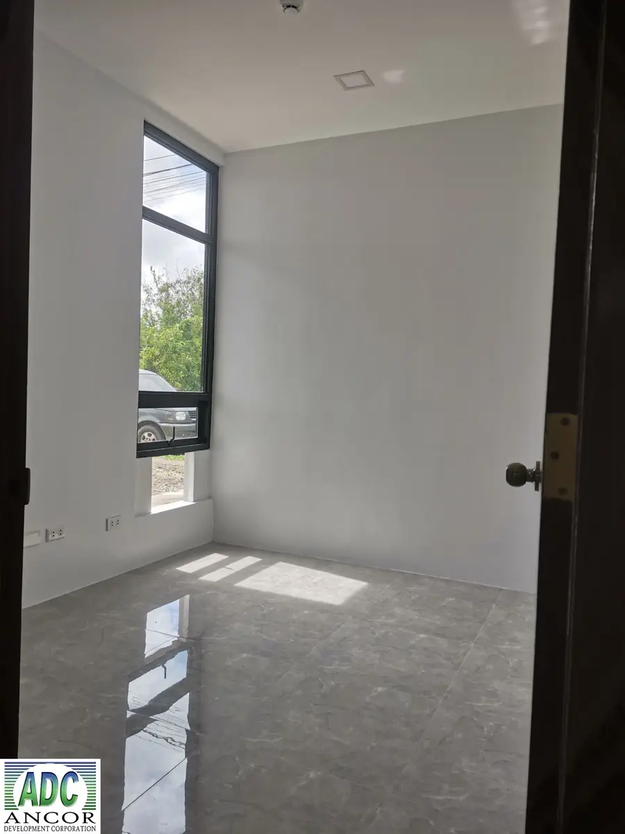 Empty bedroom with tall black framed window, white walls, wall outlets, and glossy grey tile