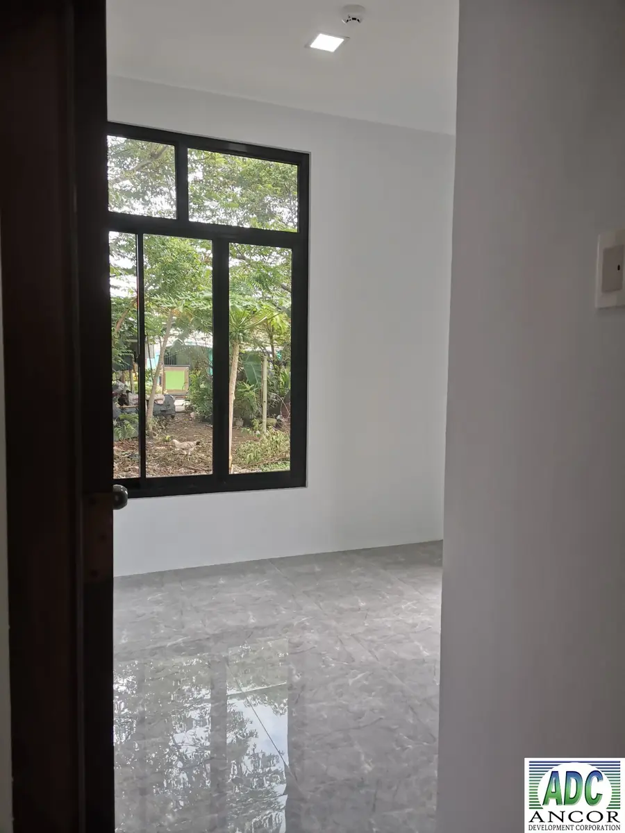 Room doorway with dark door open, black framed window looking onto trees, and grey tile floor