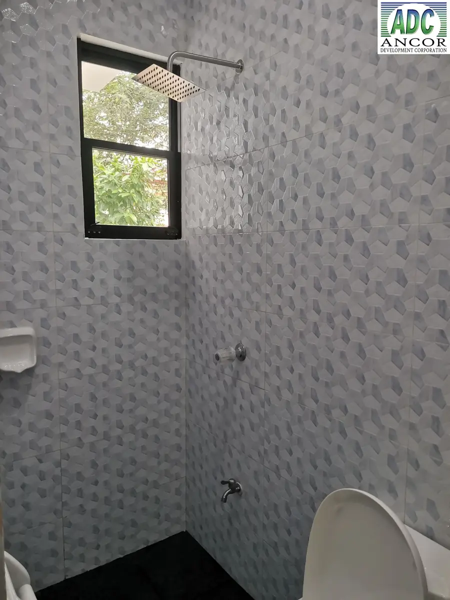 Shower area with grey patterned wall tiles, square rain shower head, and small black framed window