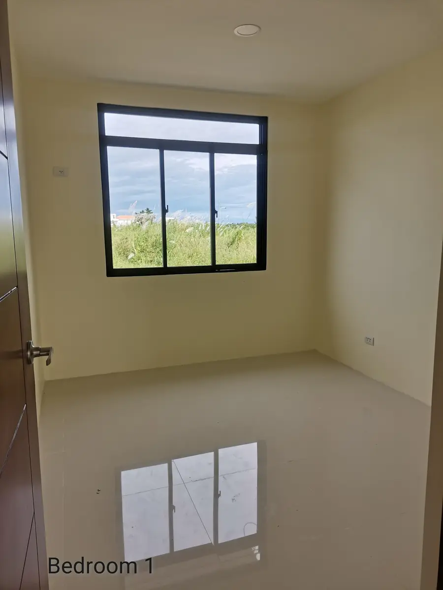Bedroom 1, empty room with cream walls, sliding window over a grass field, and glossy tile floor