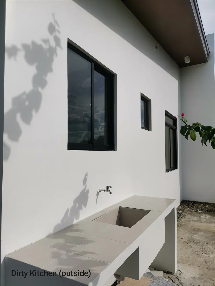 Dirty kitchen outside, tiled outdoor counter with sink and wall faucet against a white exterior wall