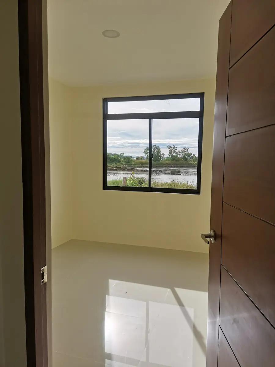 Empty bedroom with cream walls, sliding window over a river and trees, and glossy tile floor