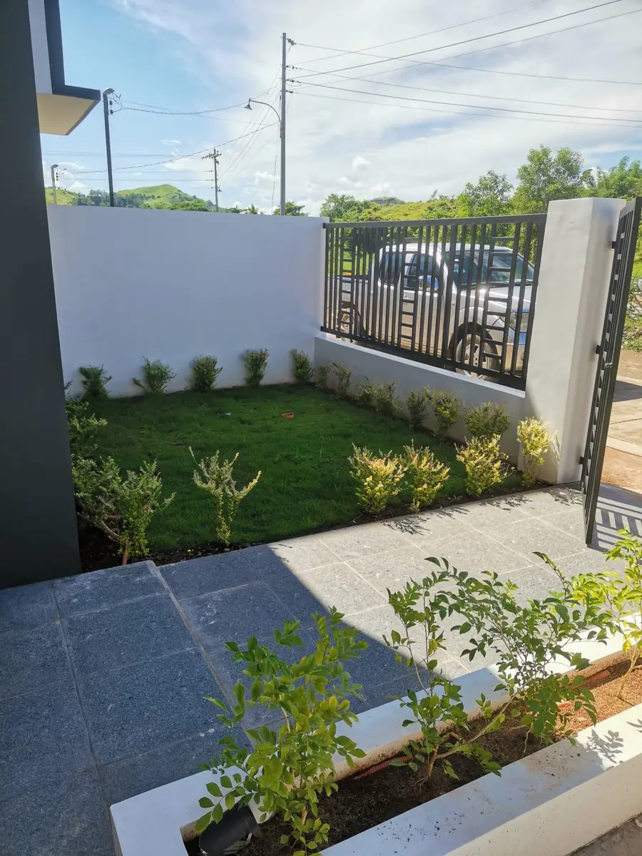 Front garden with clipped lawn, shrub border, white wall, and black steel gate open to a parked pickup