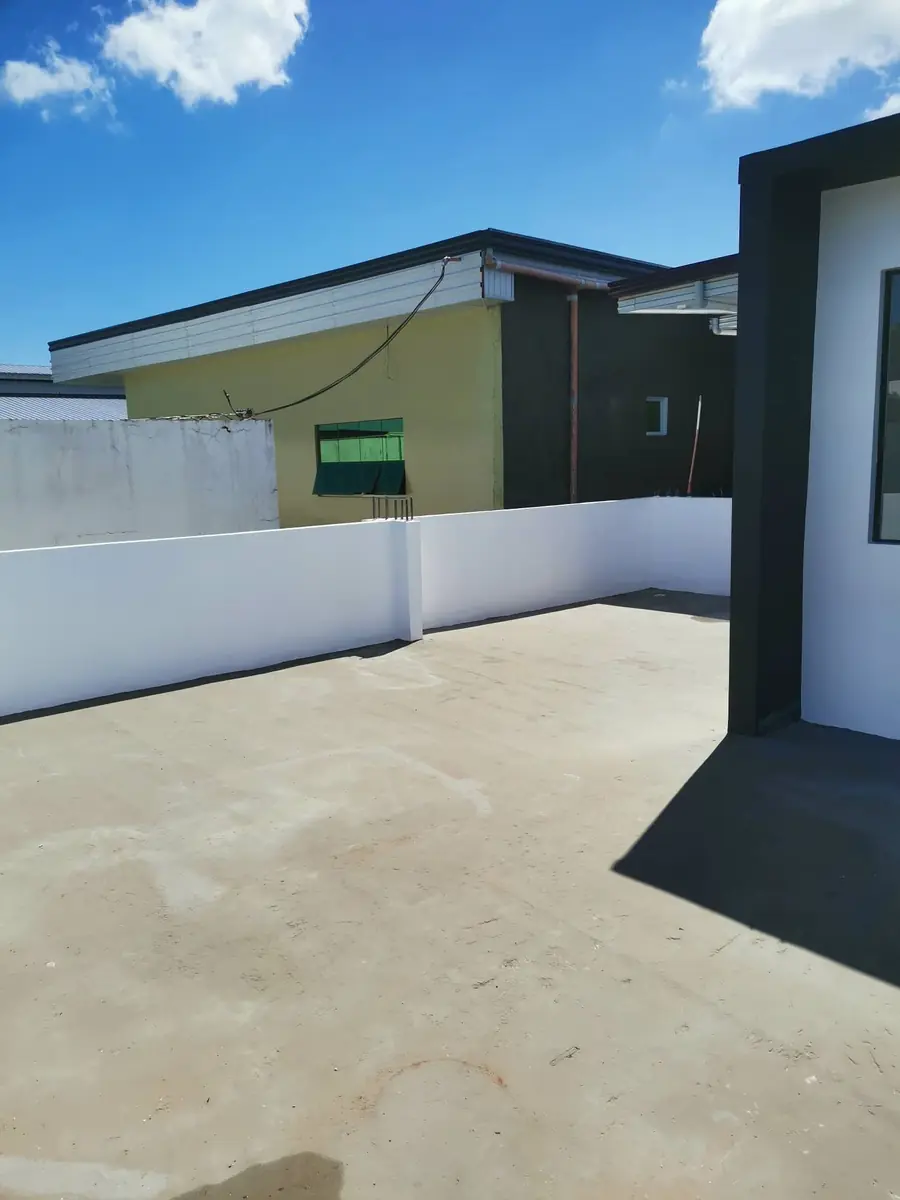 Open concrete rooftop deck bounded by a low white parapet wall, neighbouring roofs beyond