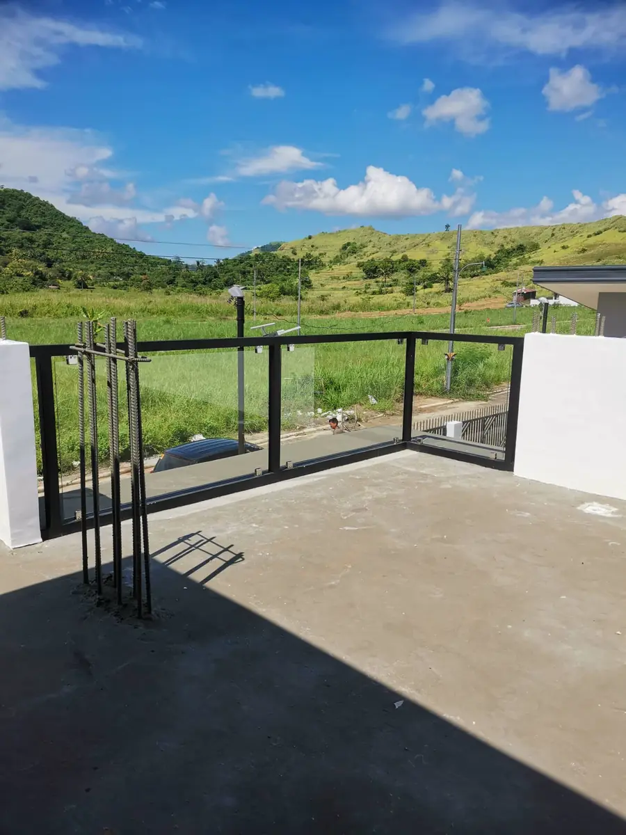 Rooftop deck with black framed glass railing overlooking green hills and rice fields