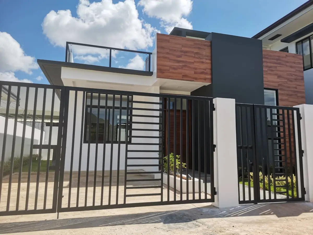Two storey house front behind a black steel gate, wood look cladding, dark grey panel, and roof deck railing