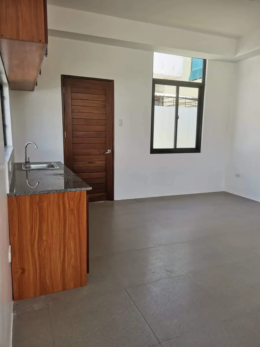 Open room with wood kitchen counter, sink, dark wood door, black framed window, and grey tile floor