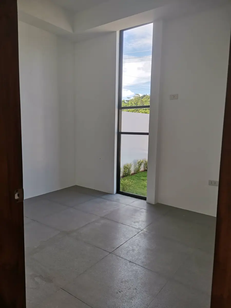 Empty room with a tall narrow window looking onto lawn, white walls, and grey tile floor