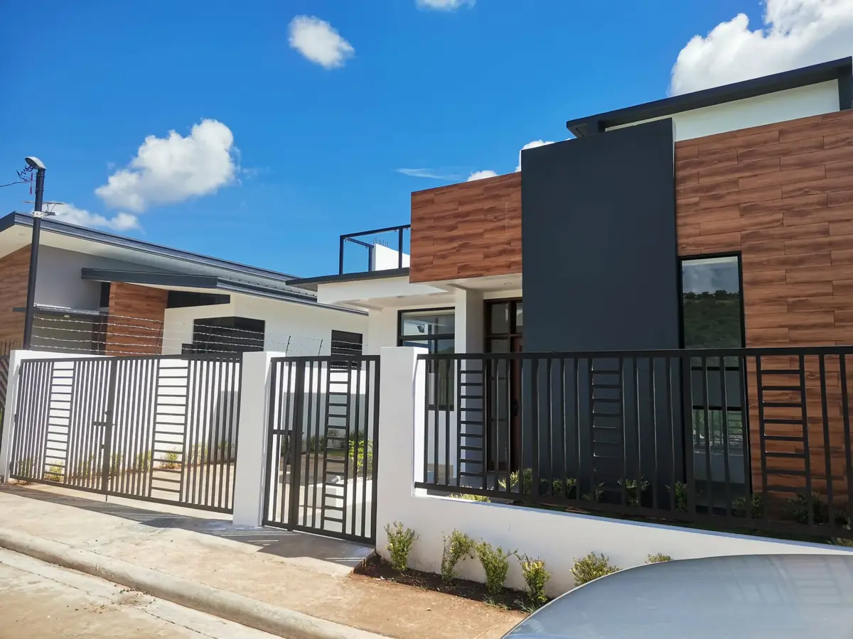 Street view of a house with wood look and dark grey cladding, roof deck, and black steel fence and gates