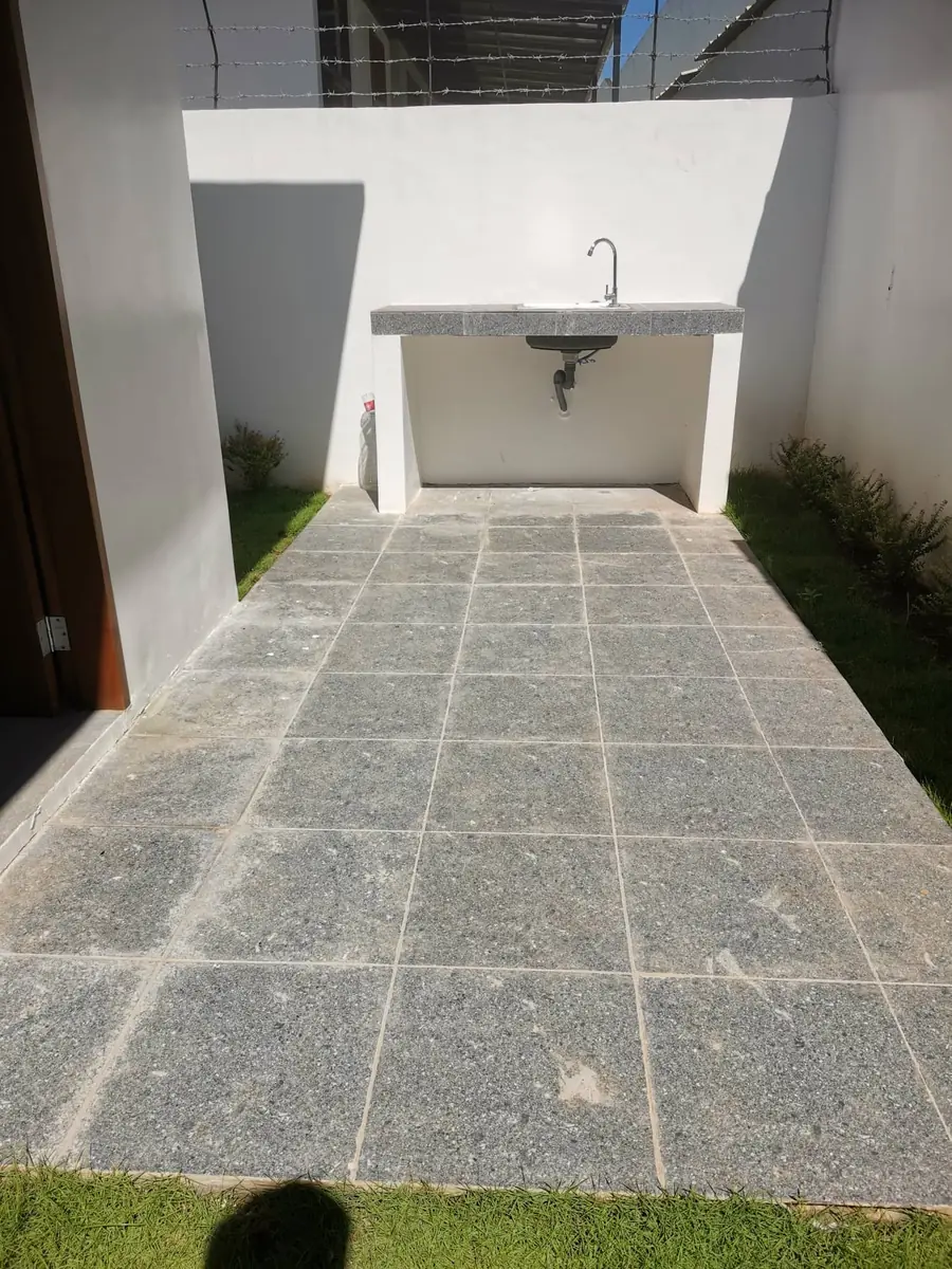 Outdoor service area with tiled counter, sink, and faucet against a white wall, granite look paving
