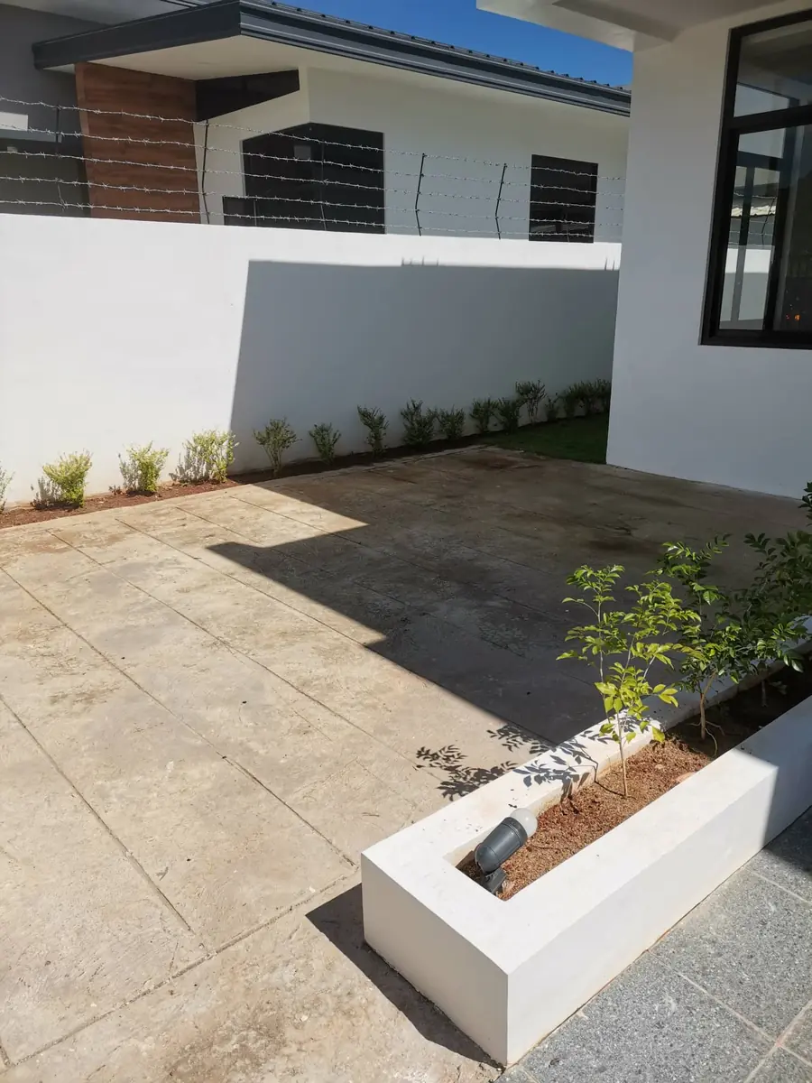 Side yard with concrete paving, white boundary wall, shrub border, and a planter box