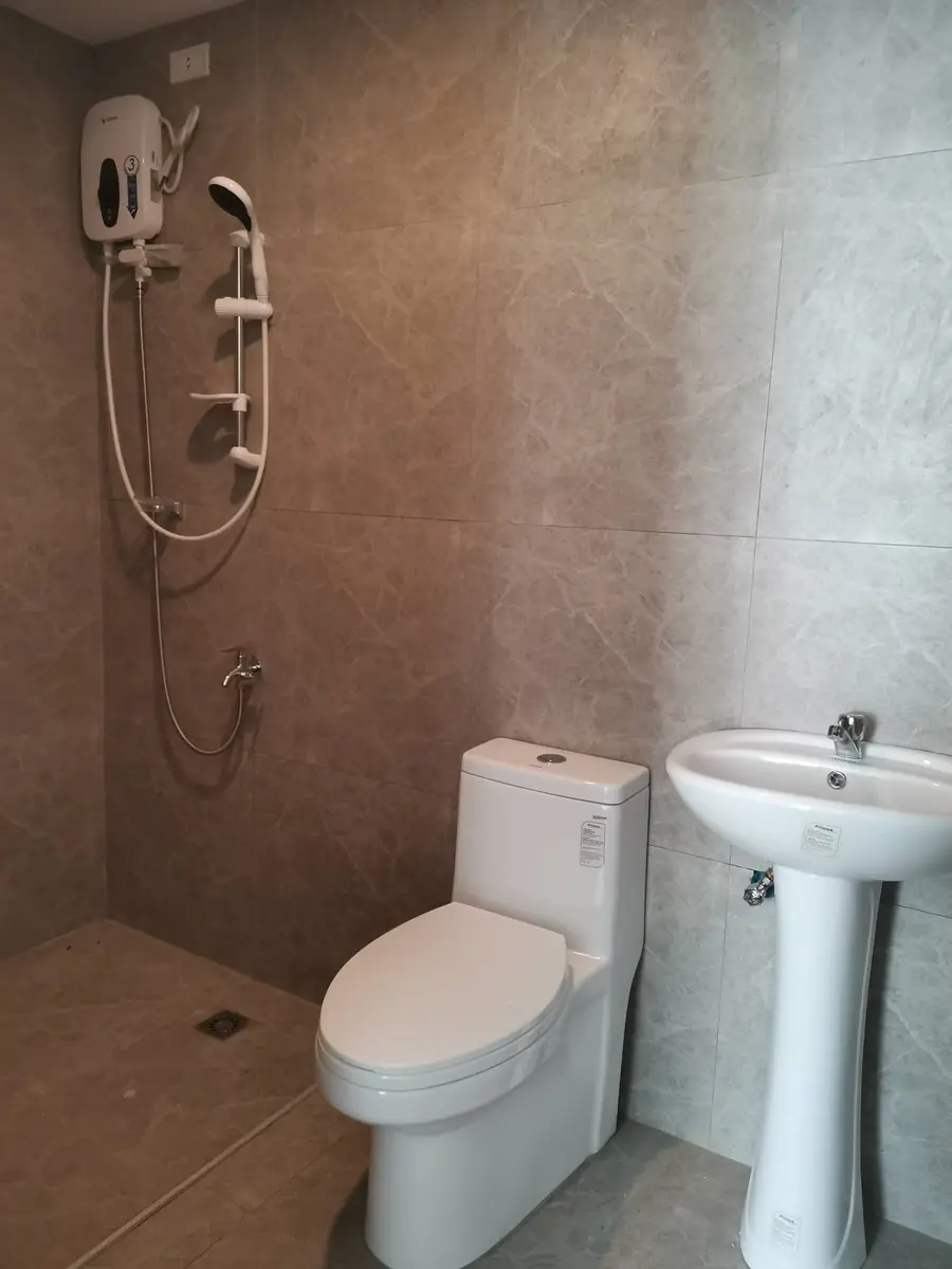 Toilet and bath with beige marble look tiles, water heater, hand shower, toilet, and pedestal sink