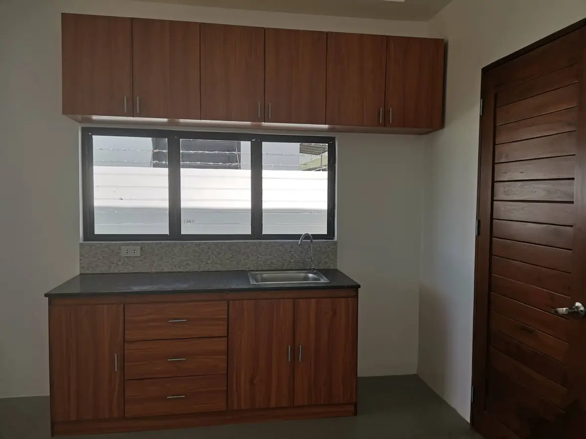Kitchen counter with dark wood cabinets, dark counter, sink, mosaic backsplash, and a sliding window