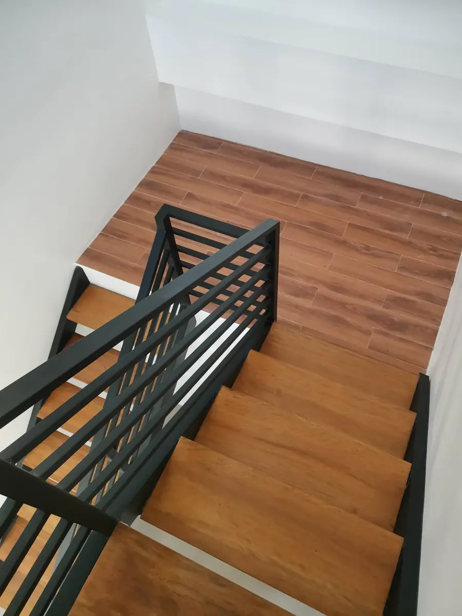 Staircase seen from above with wood treads, black steel railing, and wood look plank floor at the landing
