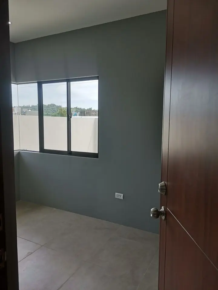 Empty bedroom with dark grey painted walls, a sliding window, and tiled floor, seen past a wood door
