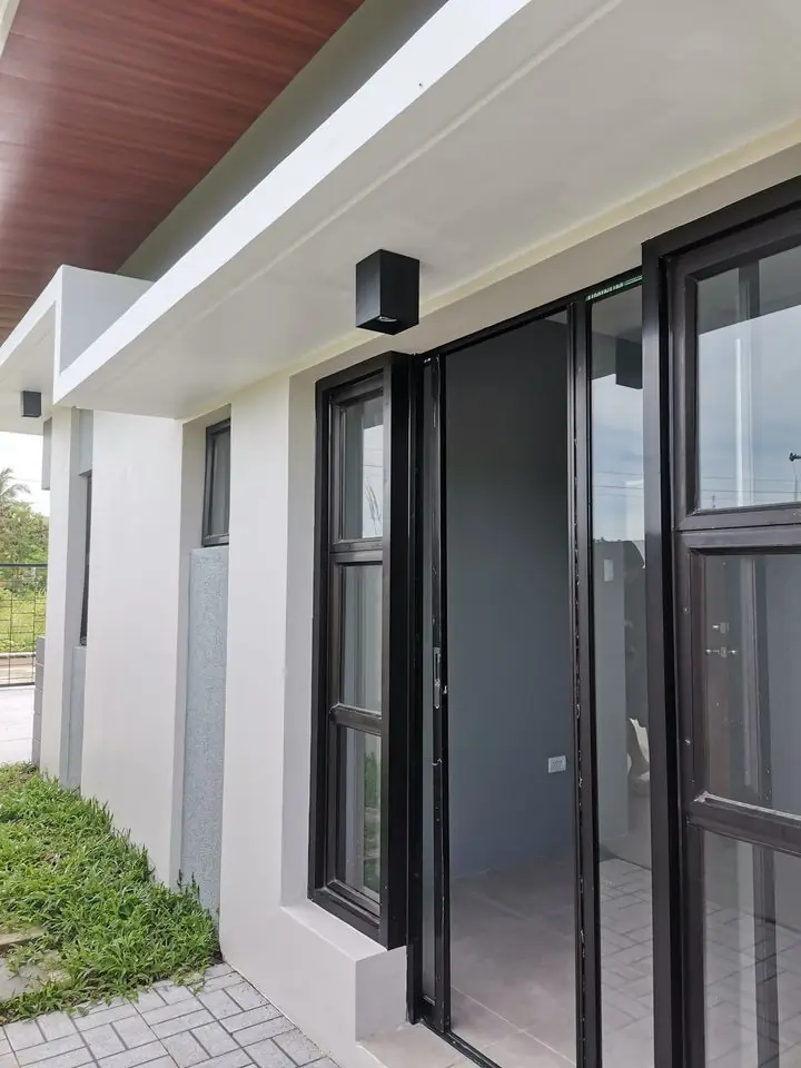 Covered entry porch with black framed glass door and windows under a wood lined ceiling
