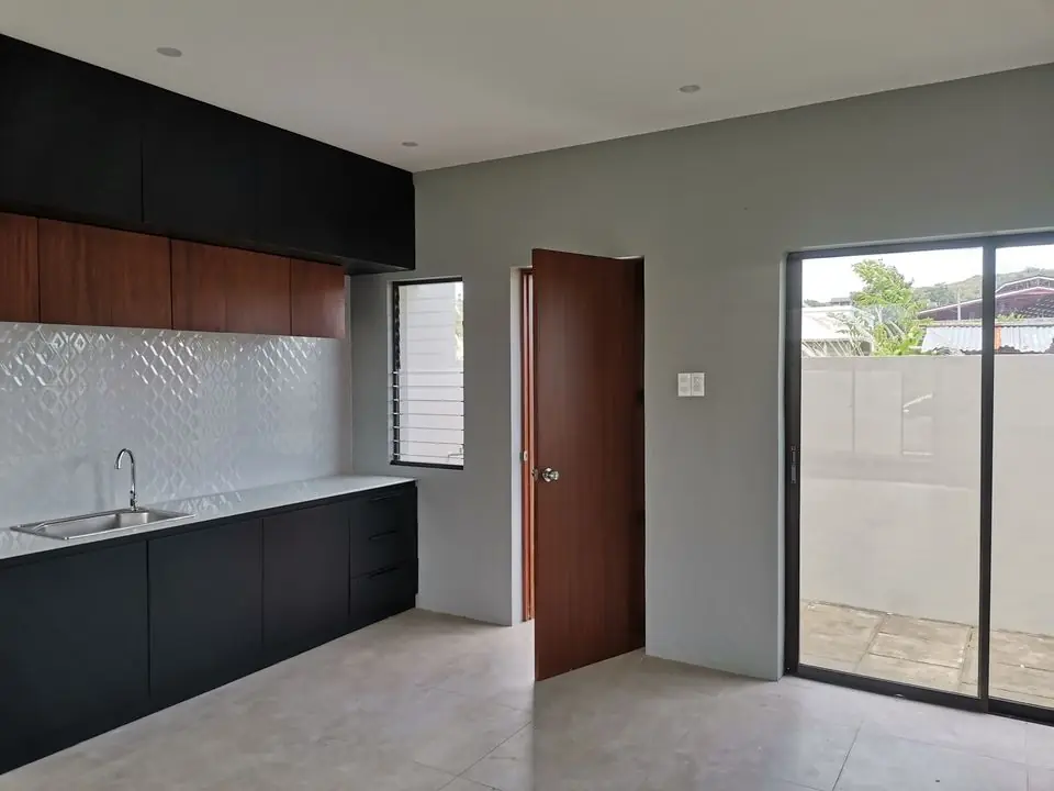 Kitchen with black lower cabinets, wood upper cabinets, sink, tiled backsplash, and a sliding glass door