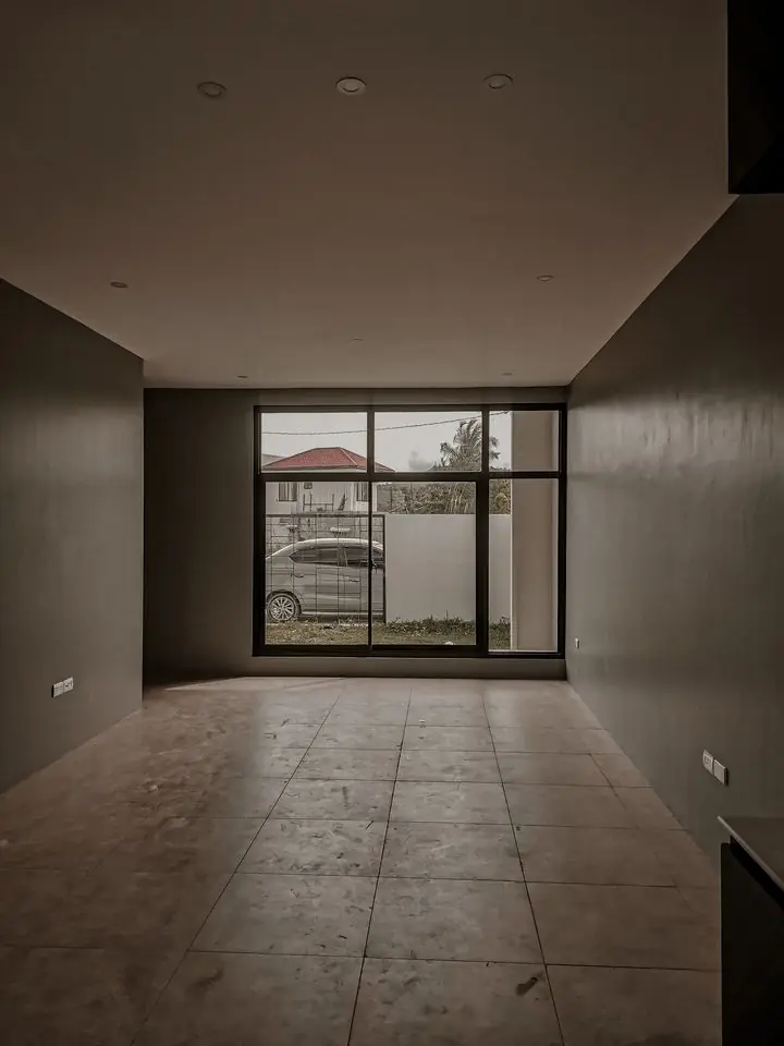 Empty living area with tiled floor and a large black framed picture window facing the street