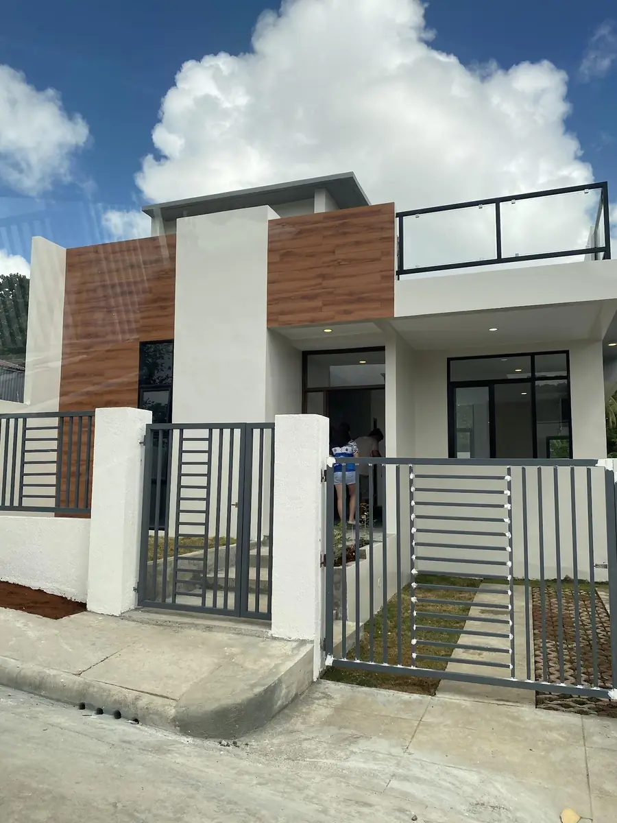 Front of a house with white and wood panel walls, roof deck railing, and grey steel gate and fence