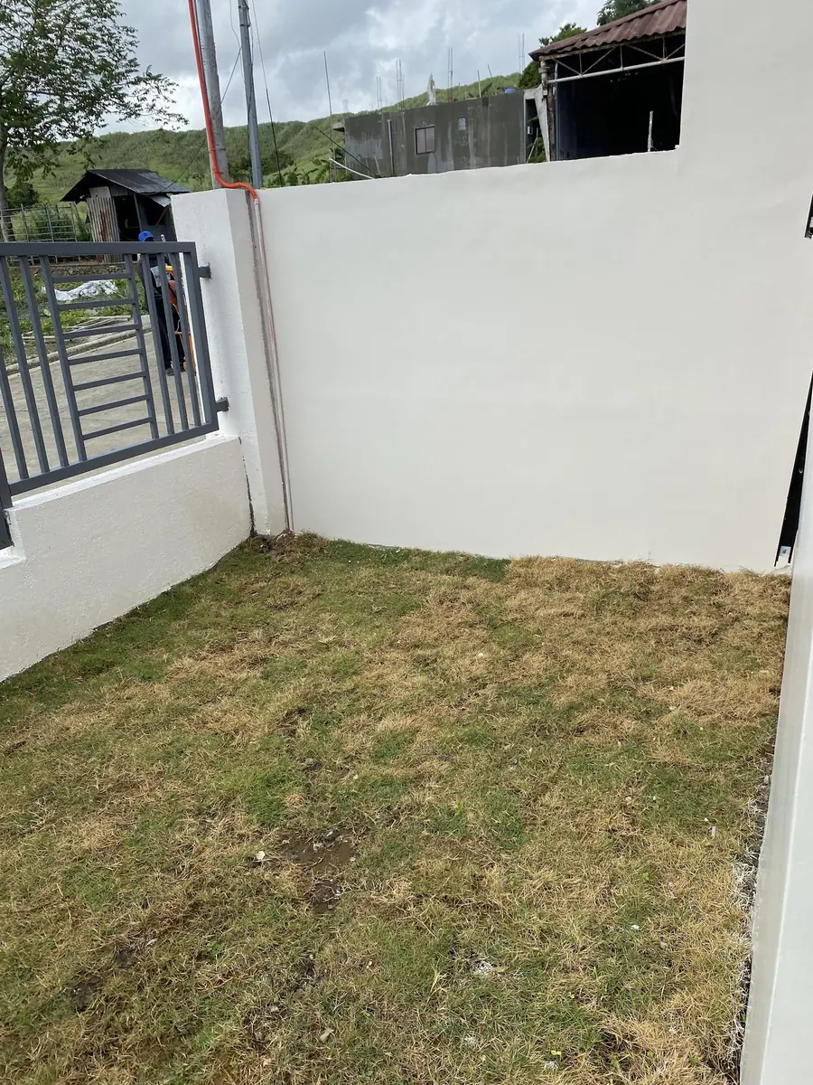 Grassed side yard enclosed by white perimeter walls and a grey steel gate