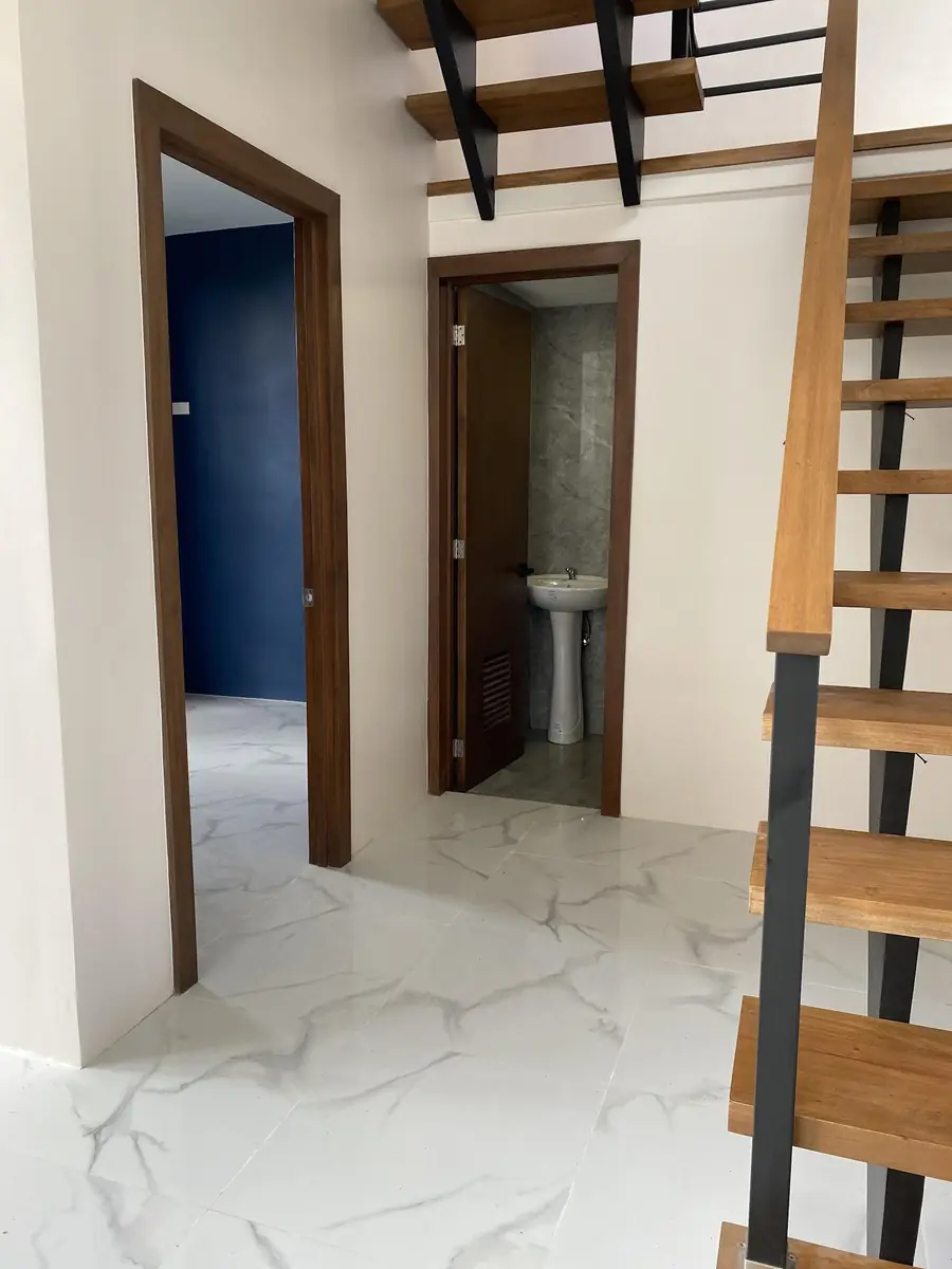 Hallway with marble look tile floor, wood door frames, a tiled toilet with pedestal sink, and open stairs