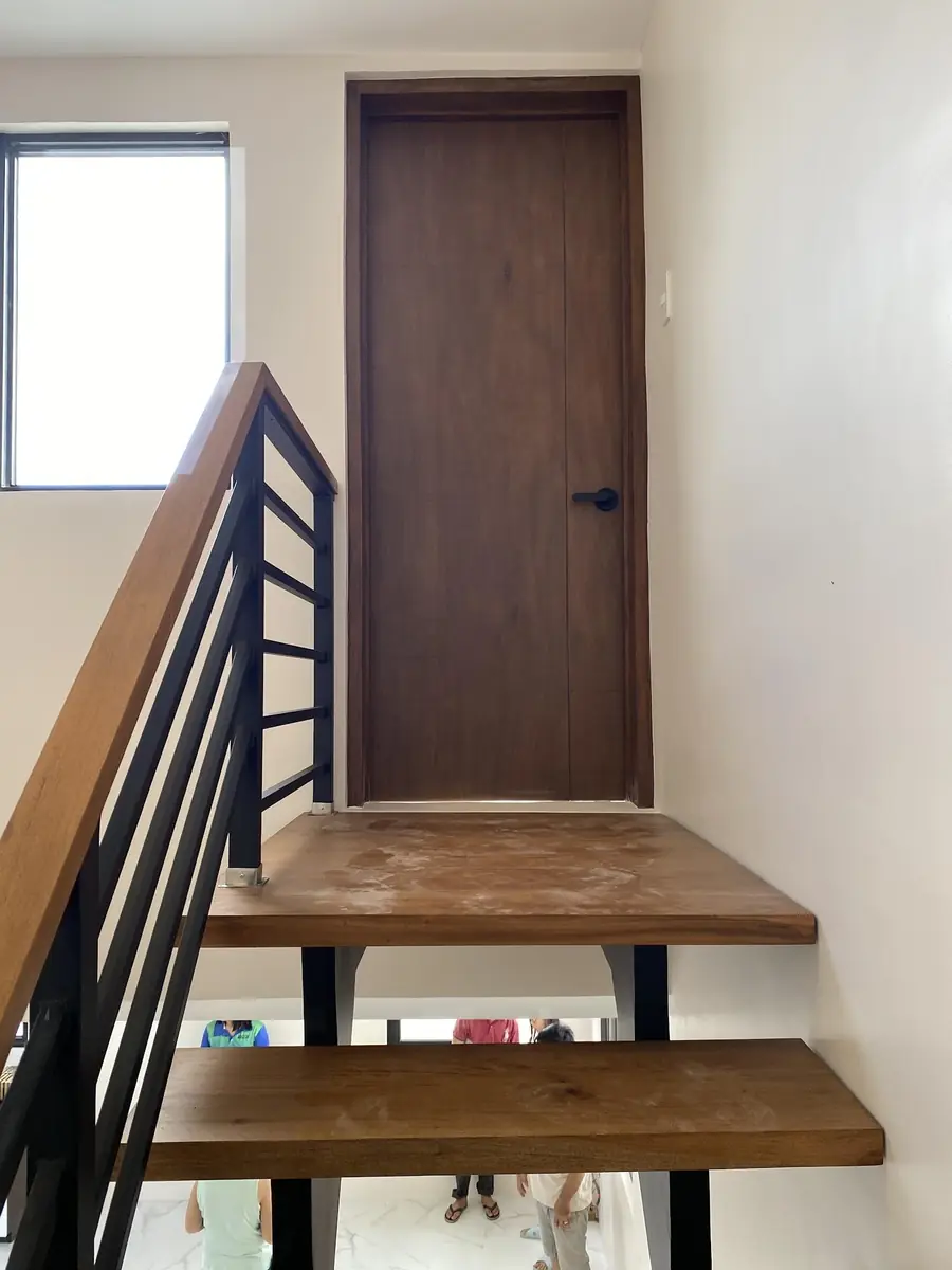 Open riser wood staircase with black steel railing leading up to a wood door on the landing