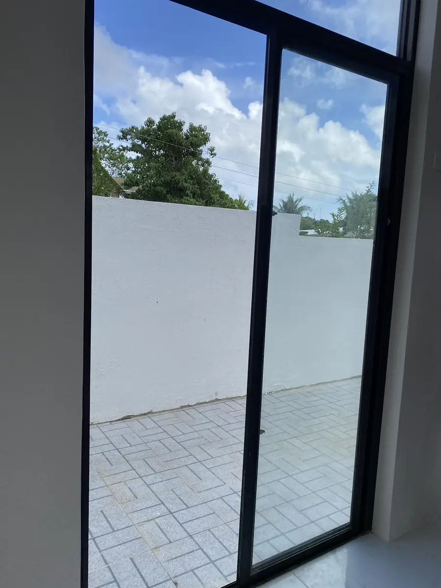 View through a black framed sliding glass door to a paved yard enclosed by a white wall