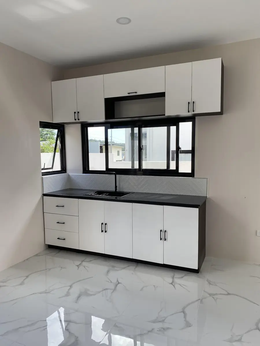 Kitchen with white cabinets, black countertop, sink, herringbone backsplash, and windows above the counter