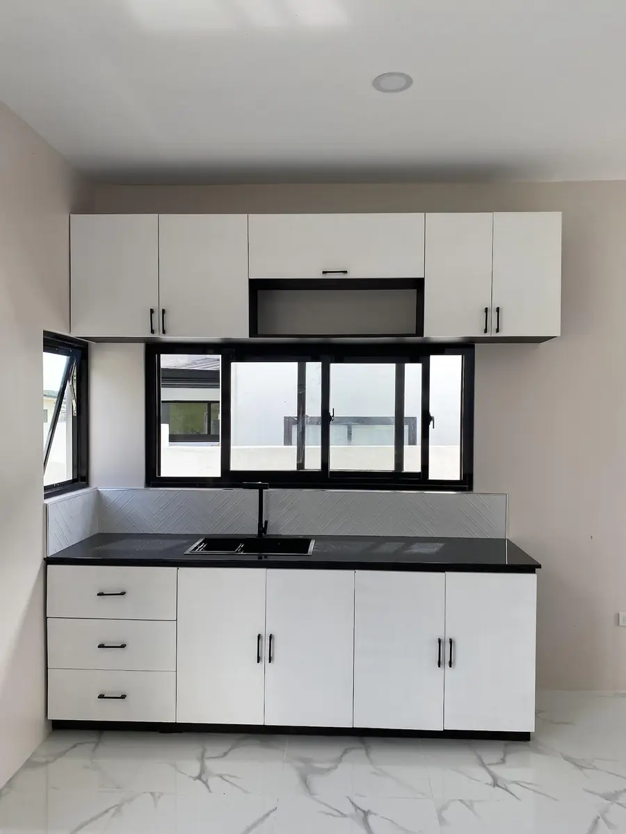 Kitchen counter with white upper and lower cabinets, black countertop, sink, and sliding windows