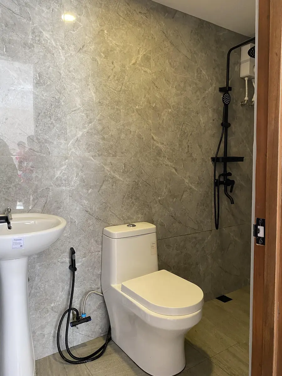 Bathroom with grey marble look tiles, pedestal sink, toilet with bidet spray, and a shower with water heater