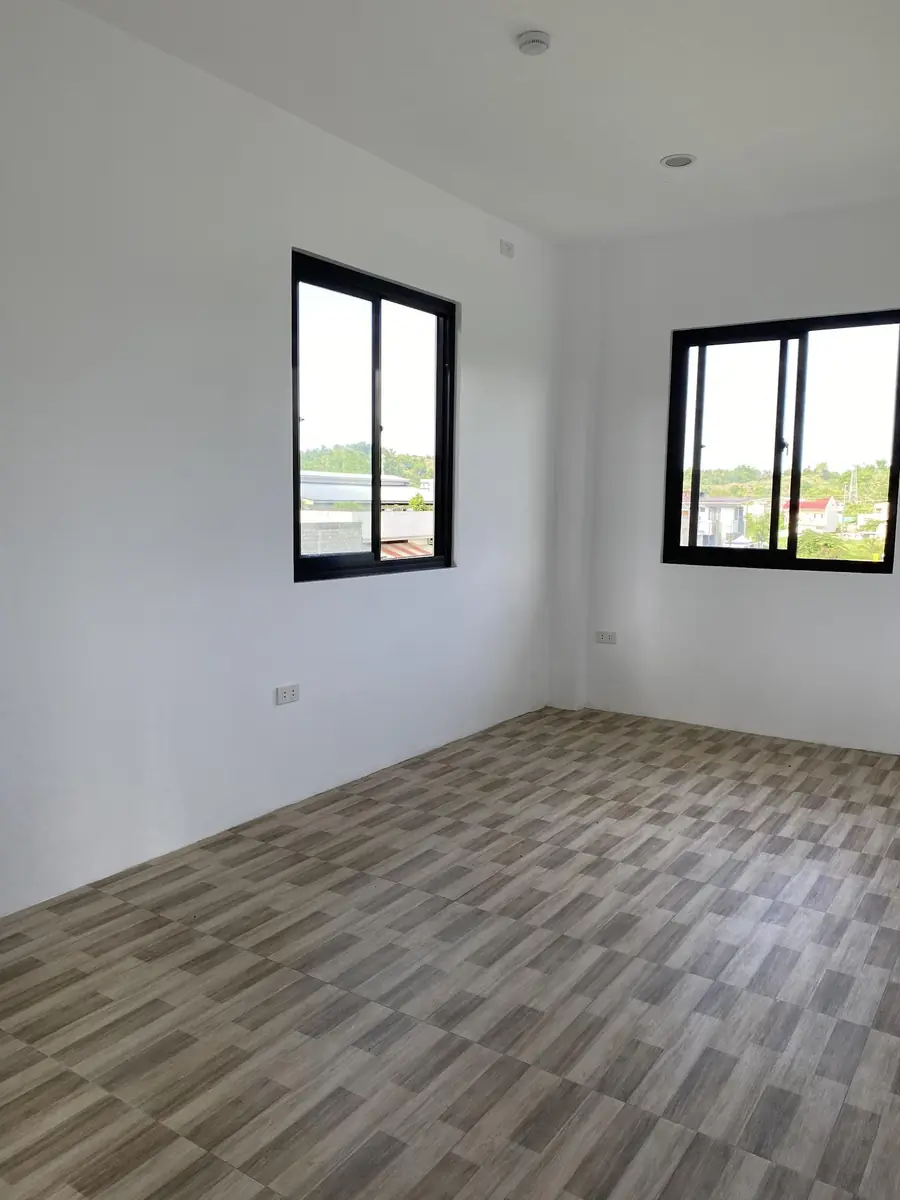 Empty bedroom with white walls, two black framed windows, and wood look tile flooring
