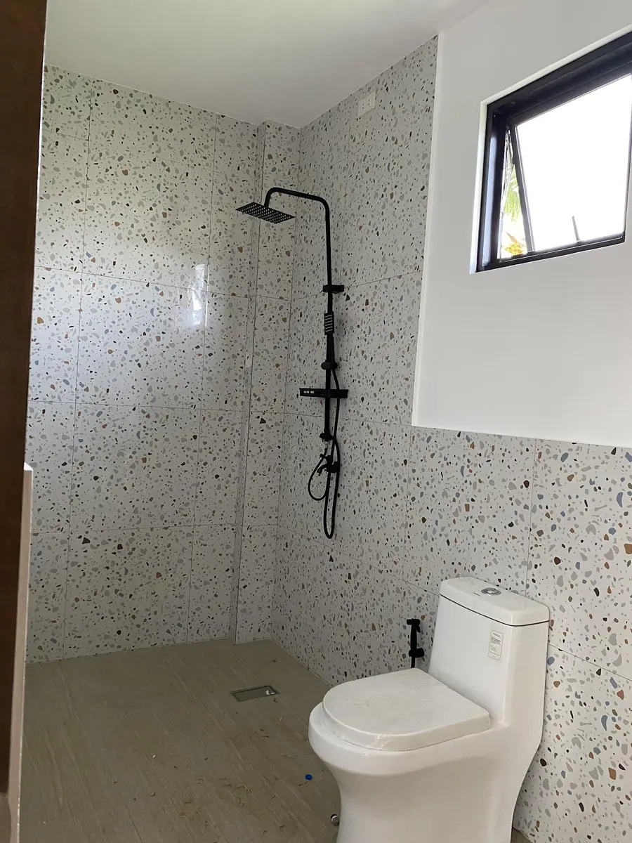 Bathroom with terrazzo look tiled walls, black rain shower, awning window, and a toilet