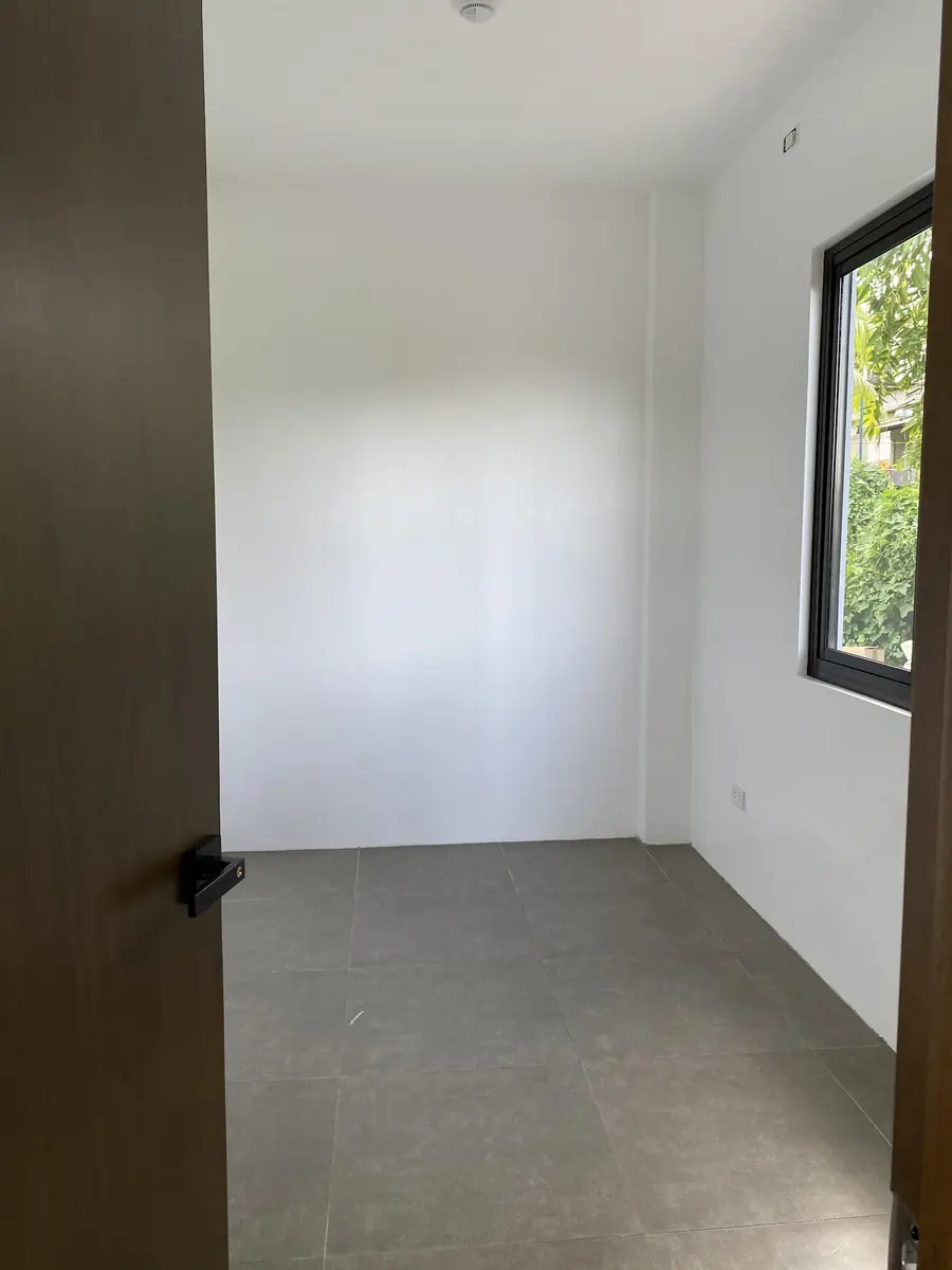 Empty room with white walls, grey tile floor, a black framed window, and a wood door