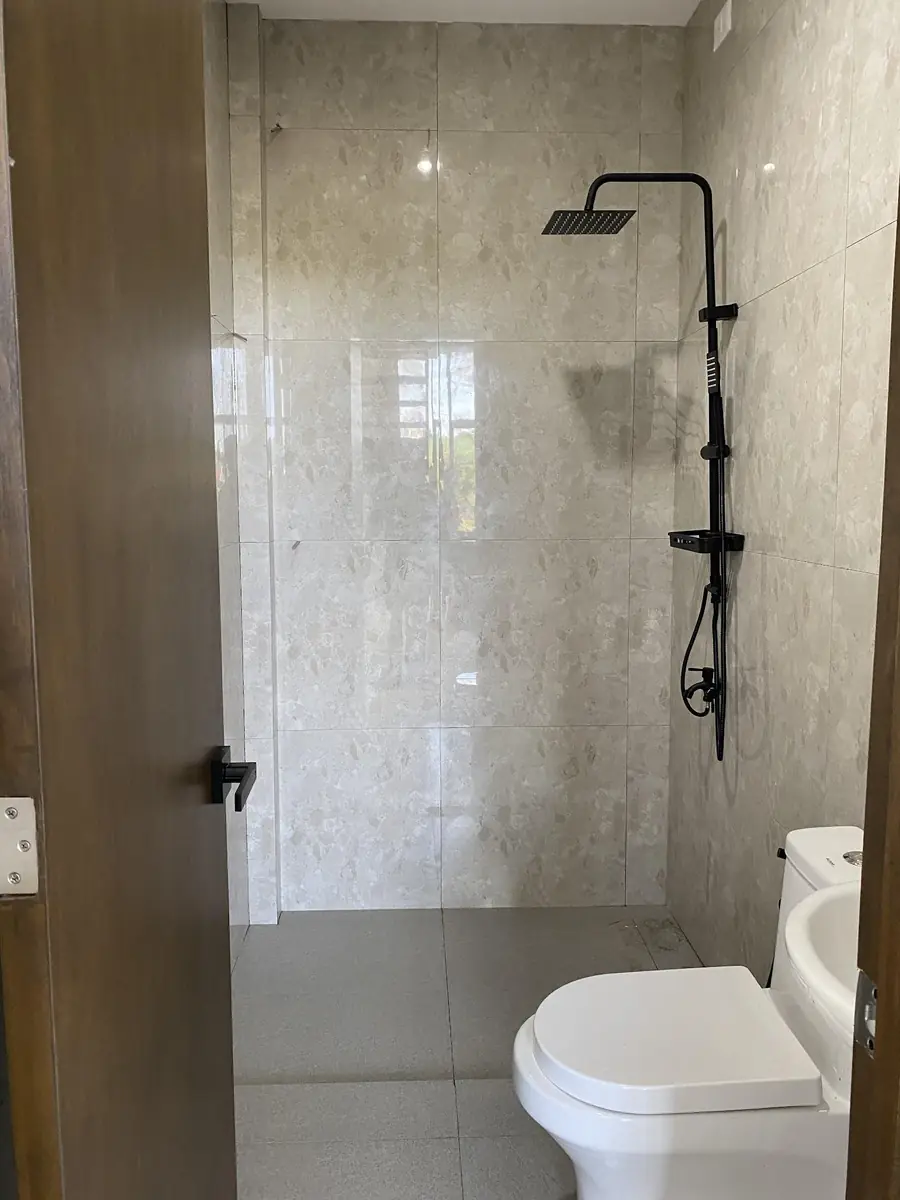 Bathroom with cream tiled walls, black rain shower and hand shower, and a toilet