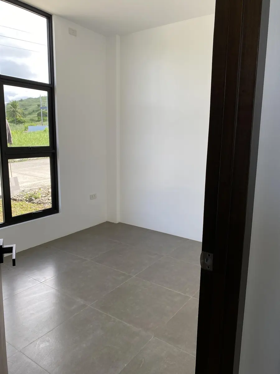 Empty room with white walls, grey tile floor, and a tall window looking out to a road and grass