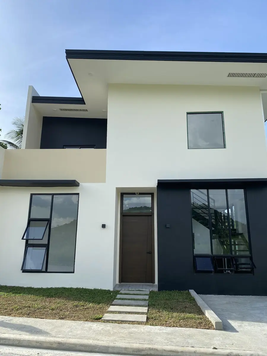 Front of a two storey house with white and dark grey walls, balcony, awning windows, and a walkway