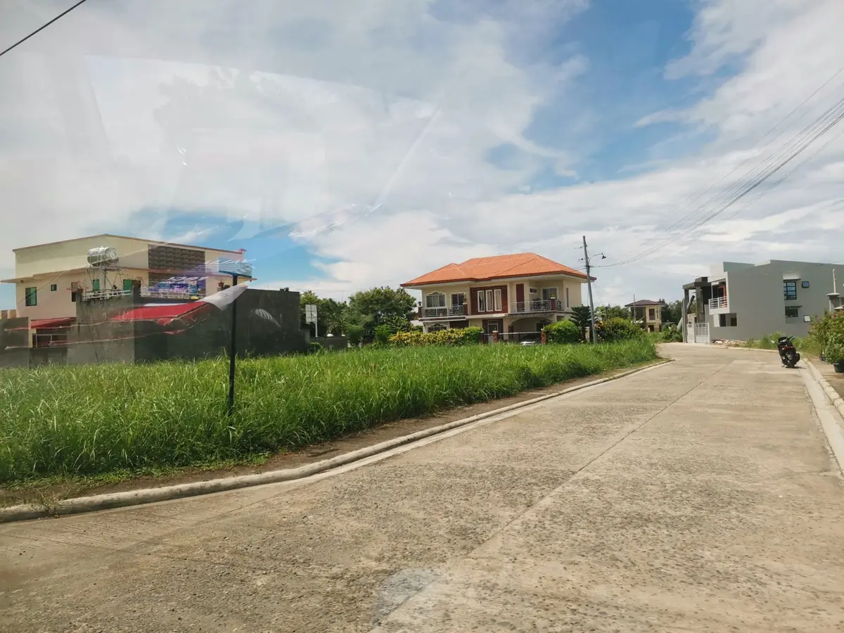 Concrete street beside a grassy lot, two storey house with an orange tiled roof and balcony across the way